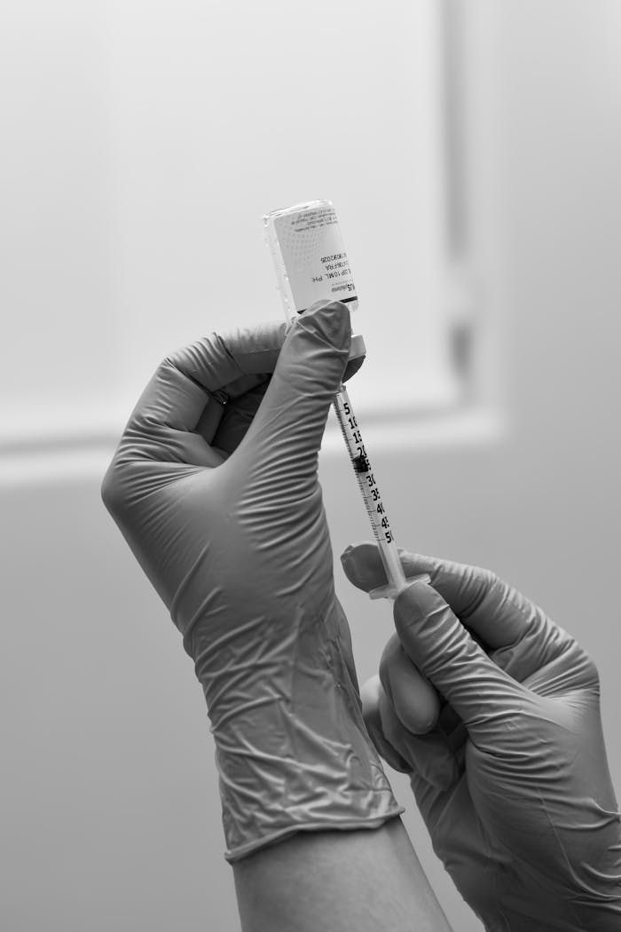 Black and white photo of gloved hands preparing a syringe with medication or vaccine.